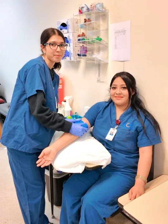 NCE Medical Assistant students practicing in blue scrubs